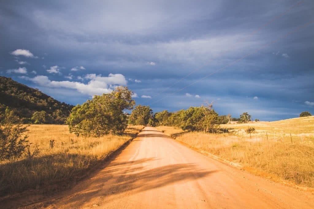 Vaga-biking // 8 Overnight Bicycle Adventures Near Sydney Henry Brydon, red dirt road, trees, blue sky, clouds, yellow fields