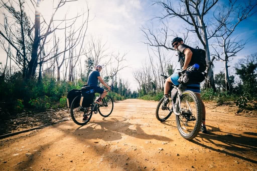 Essential Gear for Bikepacking Adventures, Henry Brydon, mountain bikes, red dirt road, trees, sky, two guys