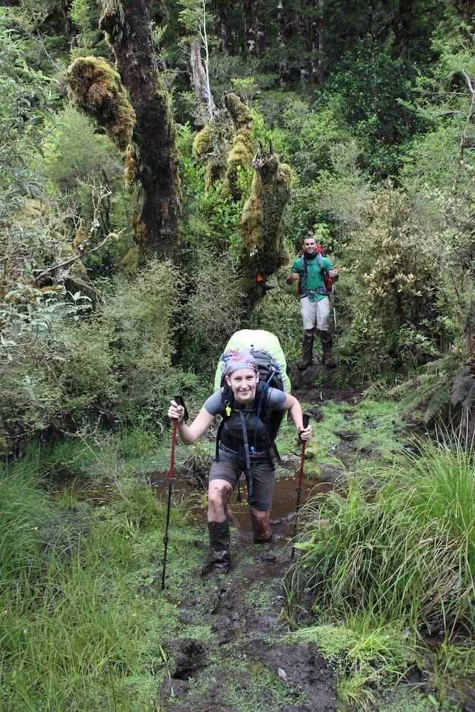 The Hardest Hike in New Zealand // Dusky Track, Tim Ashelford, photo by mitch stewart, mud, smile, hiking poles, bandana, tree stump, rain cover