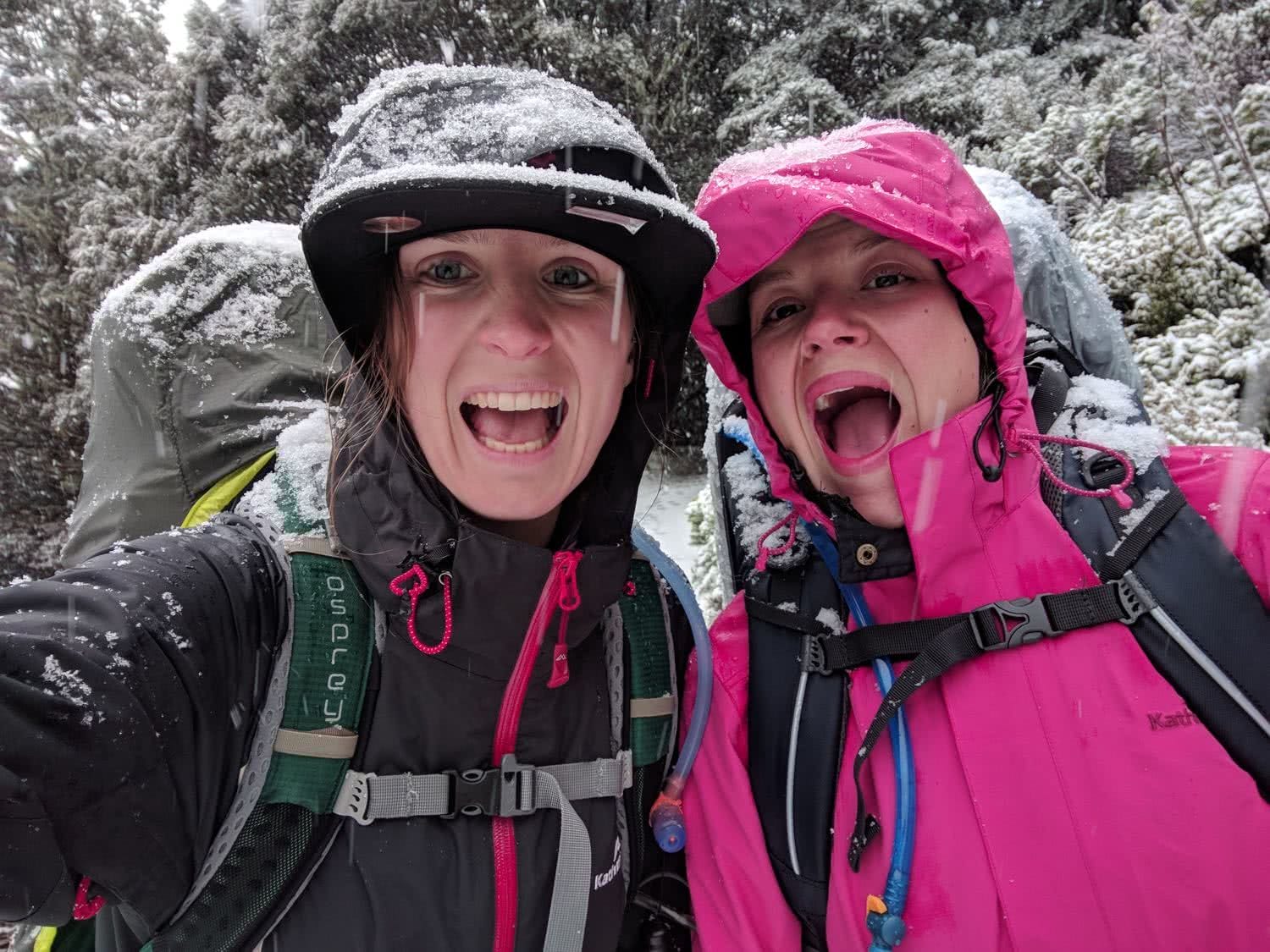 Soggy, Snowbound And Stoked // Routeburn Track (NZ), Rachel Dimond, Day 3 - Two girls in a snow storm, stoked, happy, smiles, waterproofs, backpacks, fun