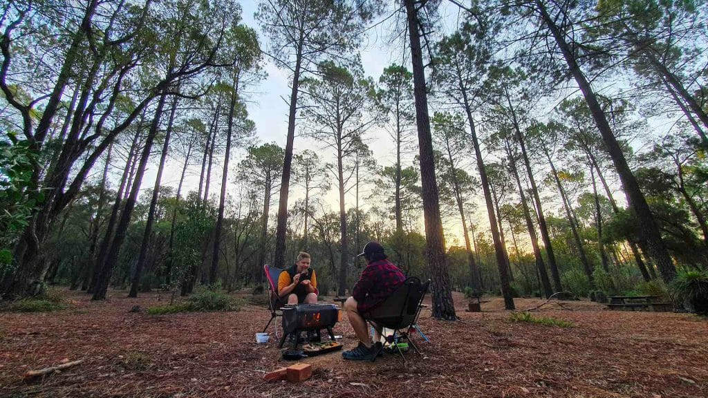 How To Cook The Ultimate Campfire Roast, Photo by Vanessa Hidayat, recipe, camping recipe, camp food, outdoor food, couple sitting in camping chairs while cooking in the forest