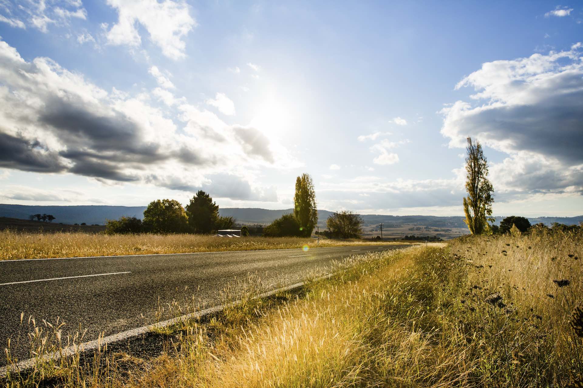 A comprehensive guide to motocamping, Adam Jones, Oxley Highway, Walcha, Sun shining over country landscape and road, Credit: Destination NSW
