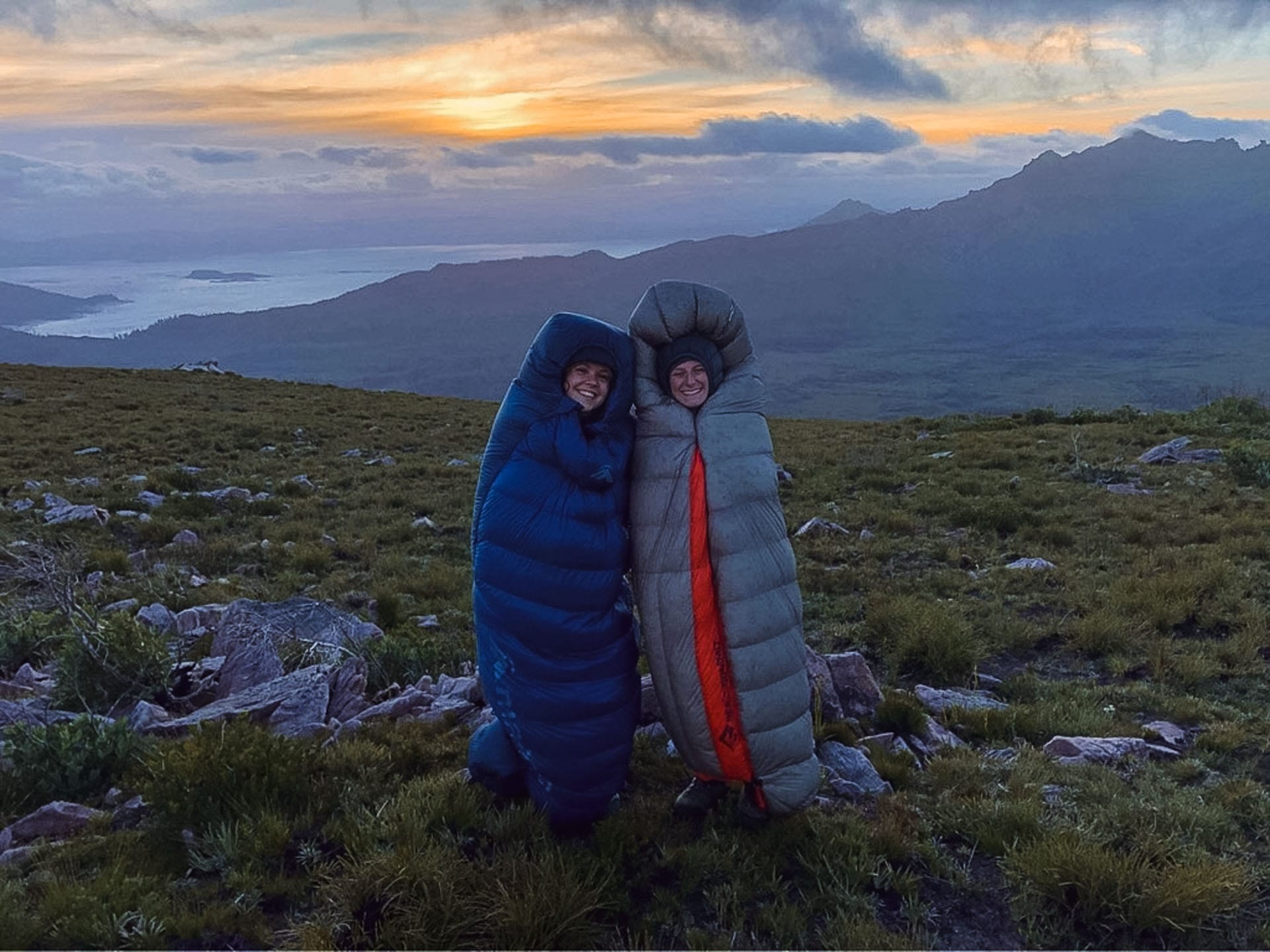Why I Calculated the Opportunity Cost of Hiking, sleeping bags, hike-in camping, camping, tent, two hikers in sleeping bags on top of mountain with sunrise