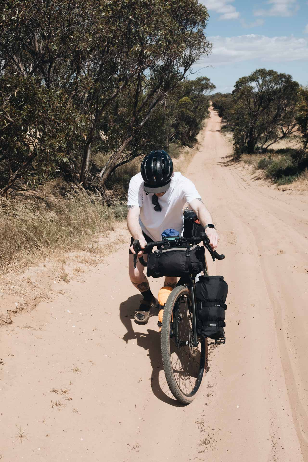 I Went Back To Basics On My Murray River Bikepacking Trip – Here’s What I Learnt, bikepacking, marmot, cyclist riding through sand with trees lining the path