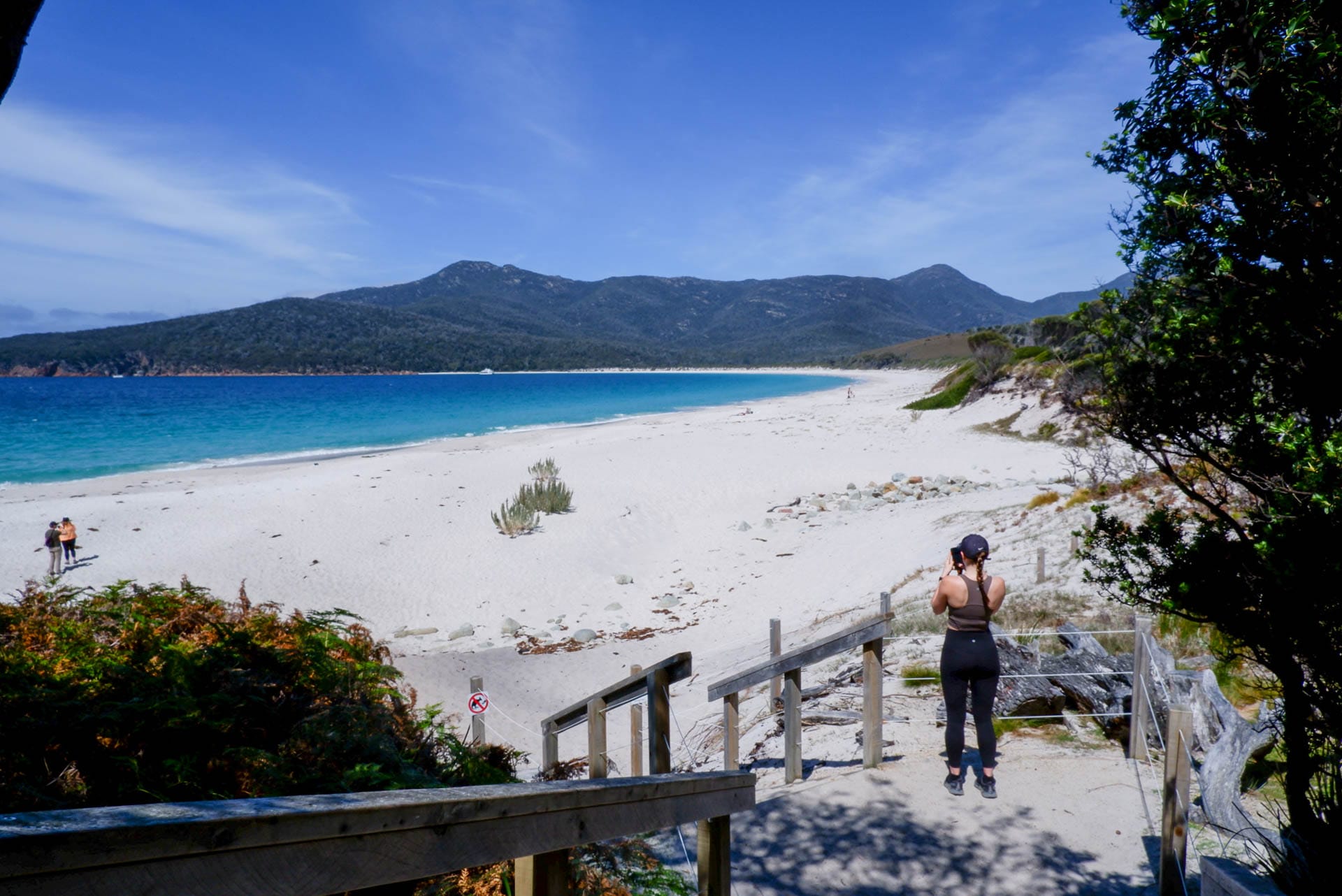 Wineglass Bay Walk – A Glorious Panoramic Trail Through Freycinet National Park, tasmania, day hike, alltrails itineraries, freycinet, woman standing above stairs leading down to the shores of wineglass bay in freycinet national park
