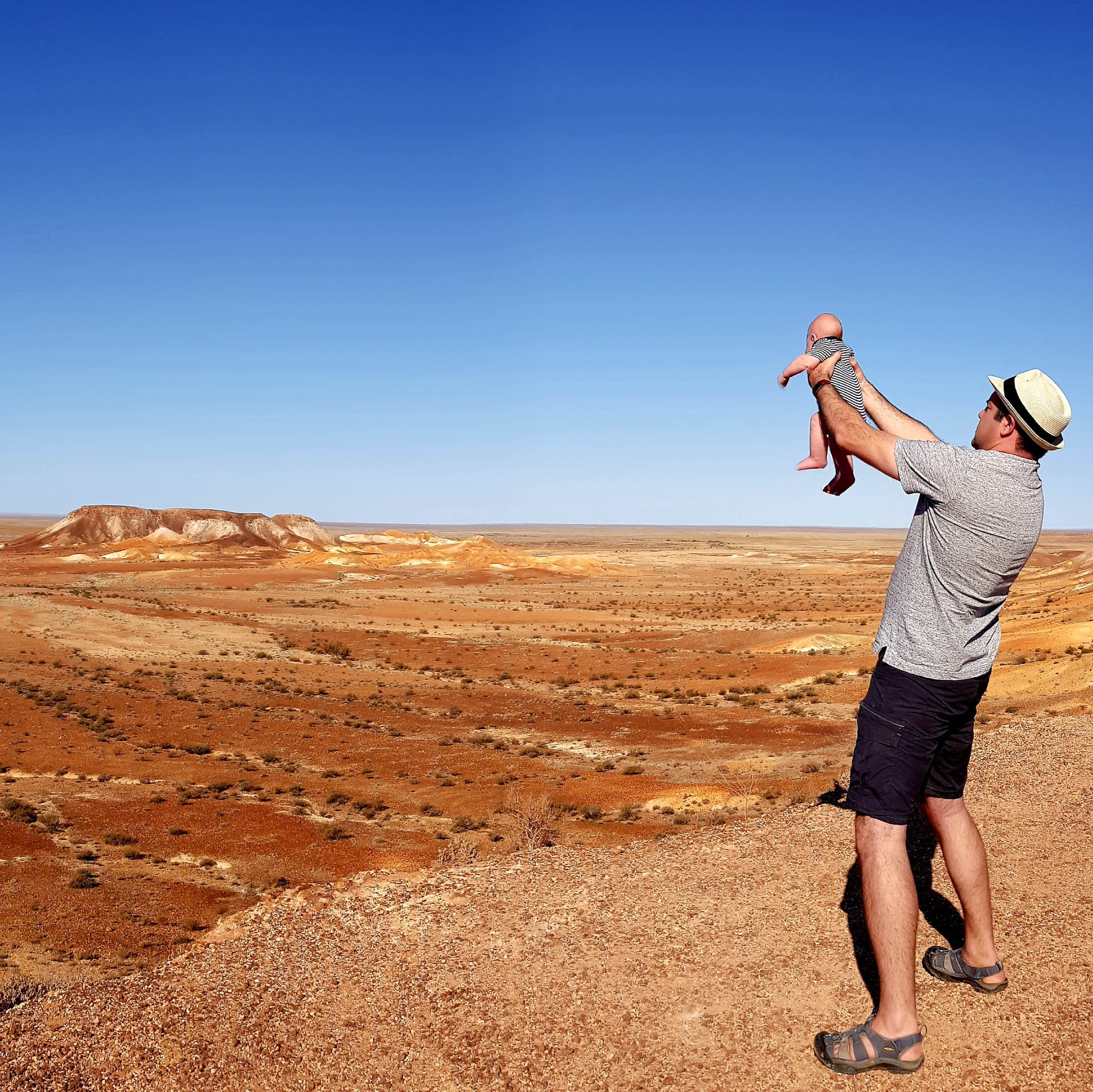 We Road Tripped From Sydney to Perth With a Three-Month-Old, road trip, van life, travelling with kids, man in a fedora holding his infant up like in the lion king overlooking the australian desert