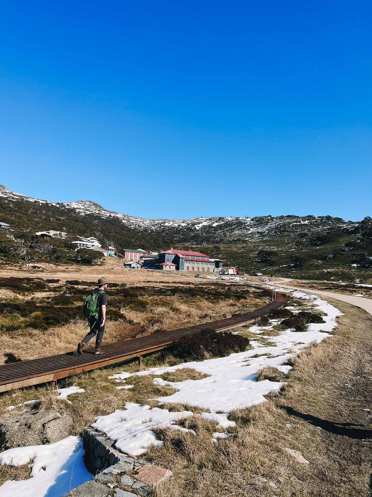 Charlotte Pass to Perisher Walk – Hiking the Newest Stage of the Snowies Alpine Walk in Kosciuszko National Park, nsw hikes, Photo by Kate Donald, alpine, back country, day hike, hiker on snowy trail at kosciuszko with accommodation in background