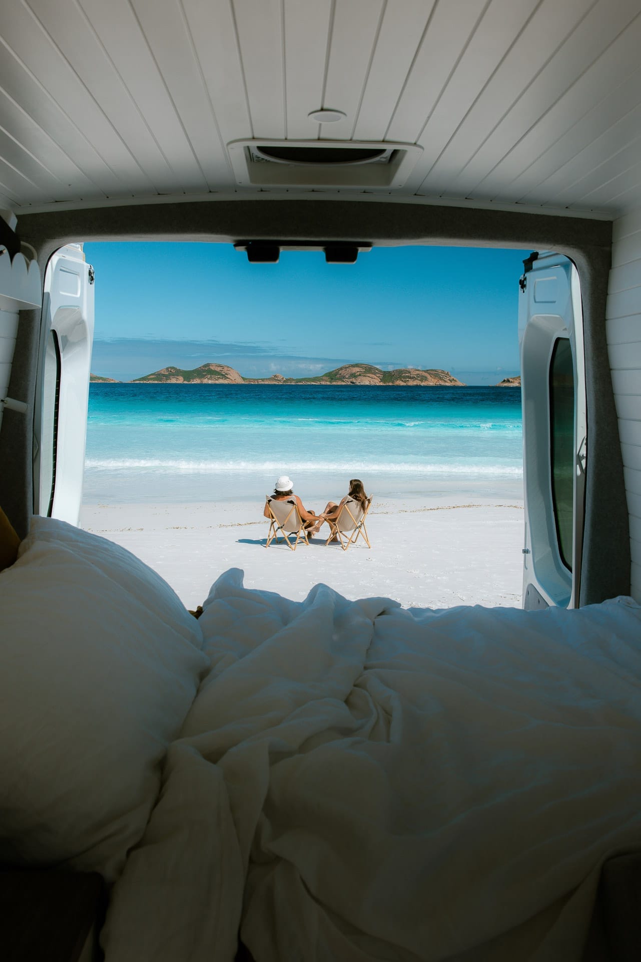 Why April is My Favourite Month For a Road Trip, Photo supplied by Camplify and taken by Hayley Andersen, holidays, easter, campervan, van life, two people sitting in chairs by the beach, blue water