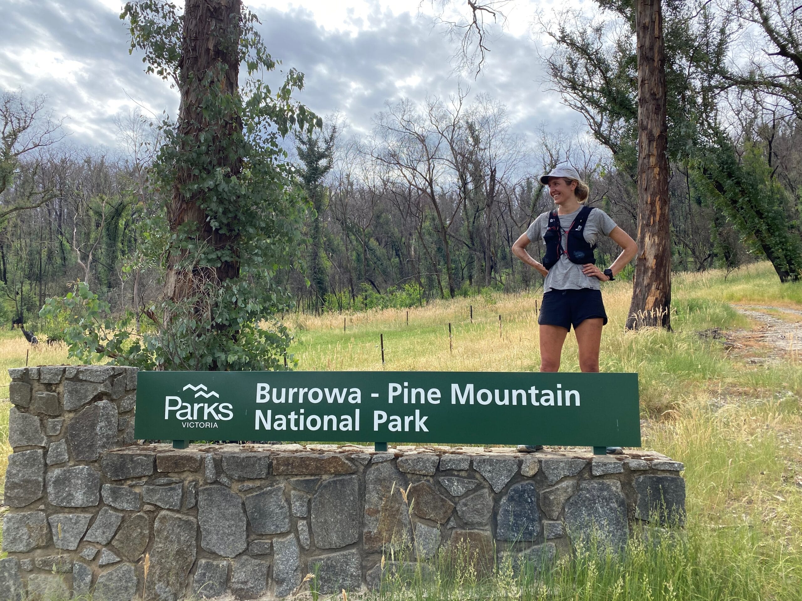 Woman stands on a sign marking the entrance to Burrowa-Pine National Park.