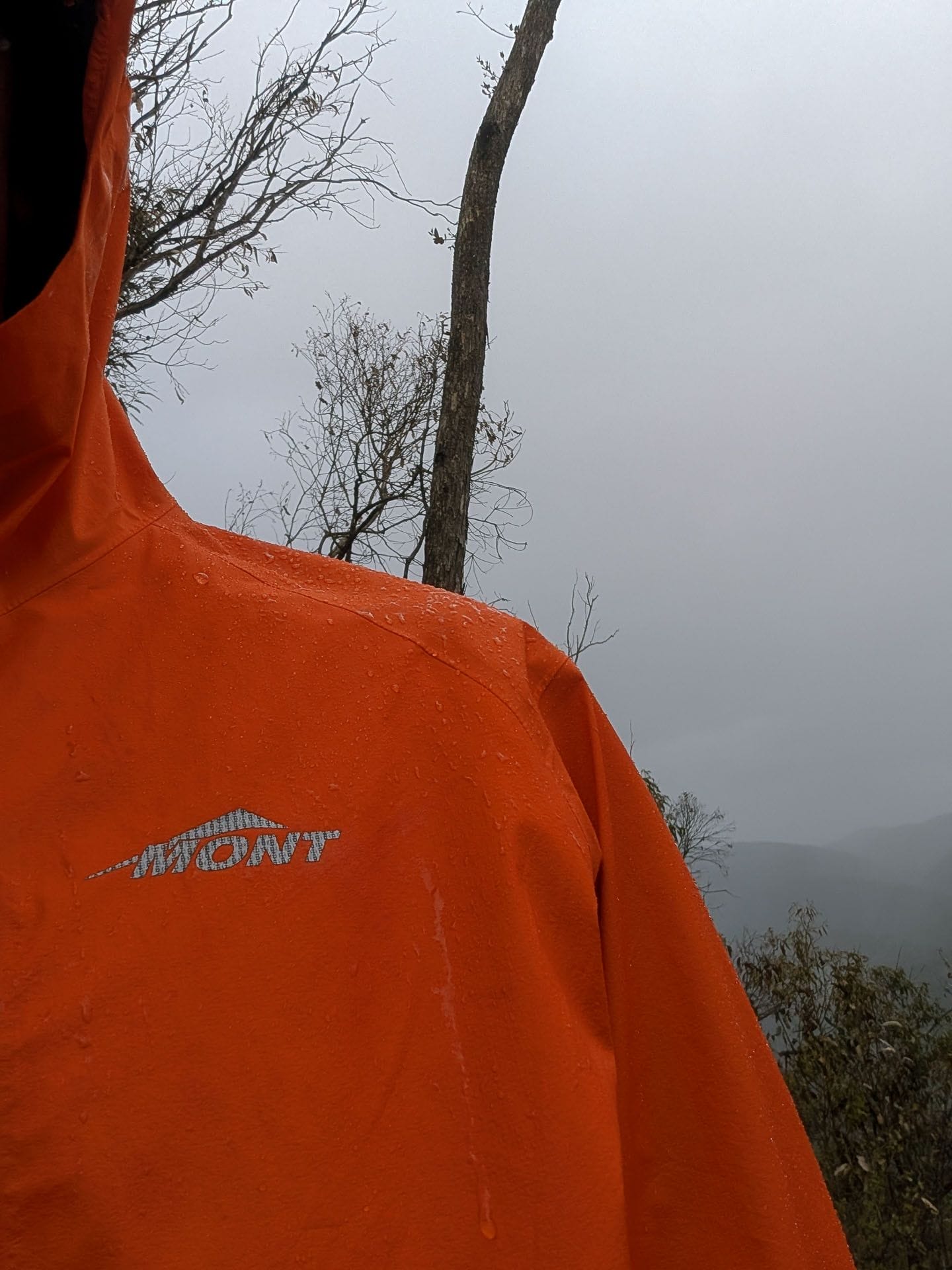 Mont Lightspeed Rain Jacket, by Ryan and Emily, orange rain jacket, water droplets, PFA-free DWR coating, overcast sky, outdoor hiking gear, waterproof