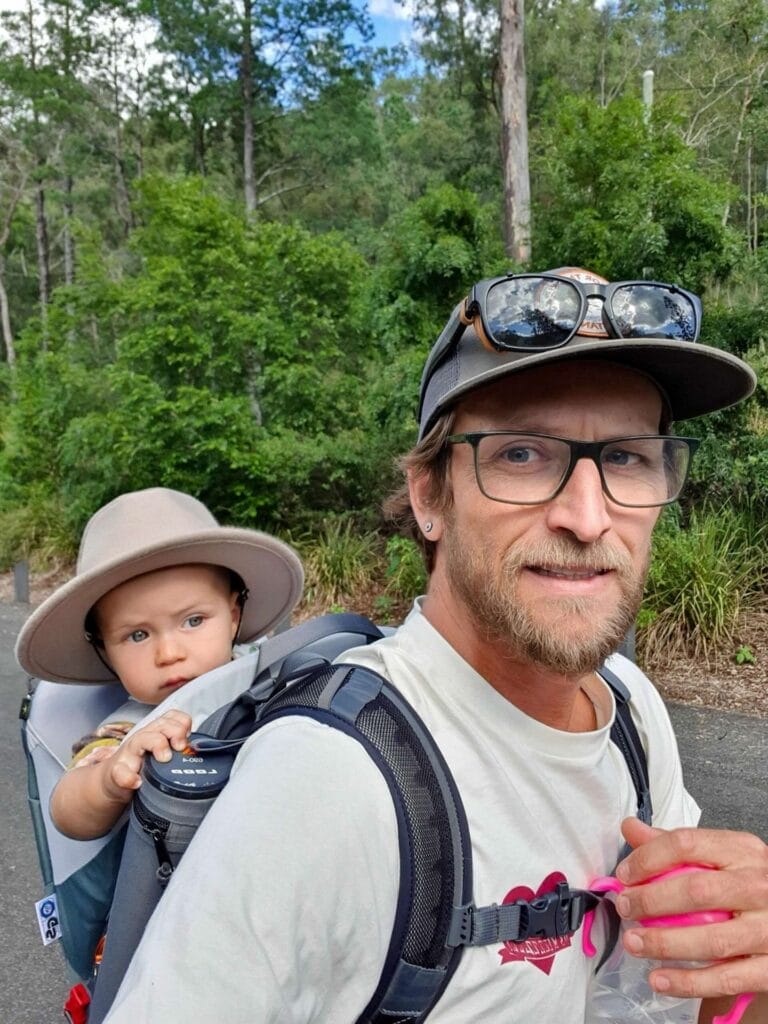 Father and son, baby carrier, forest trail, walking, smiling, outdoors, nature, green trees, parenting, family adventure, risk management