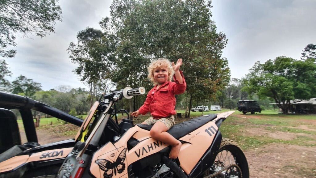 Young boy, dirt bike, adventure, risk, outdoor, family travel, camping, smiling, waving, curly hair, VAHNA, SKDA, by Josh