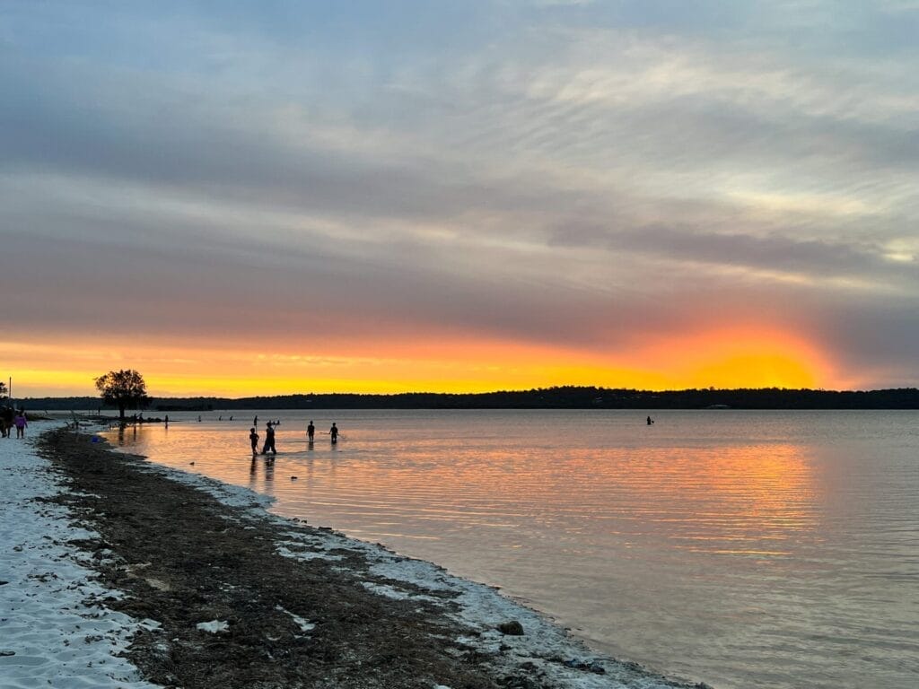 Herron Point, by Lisa Ikin, sunset, Peel-Harvey Estuary, people wading, sandy beach, calm water, vibrant colors, sky reflection