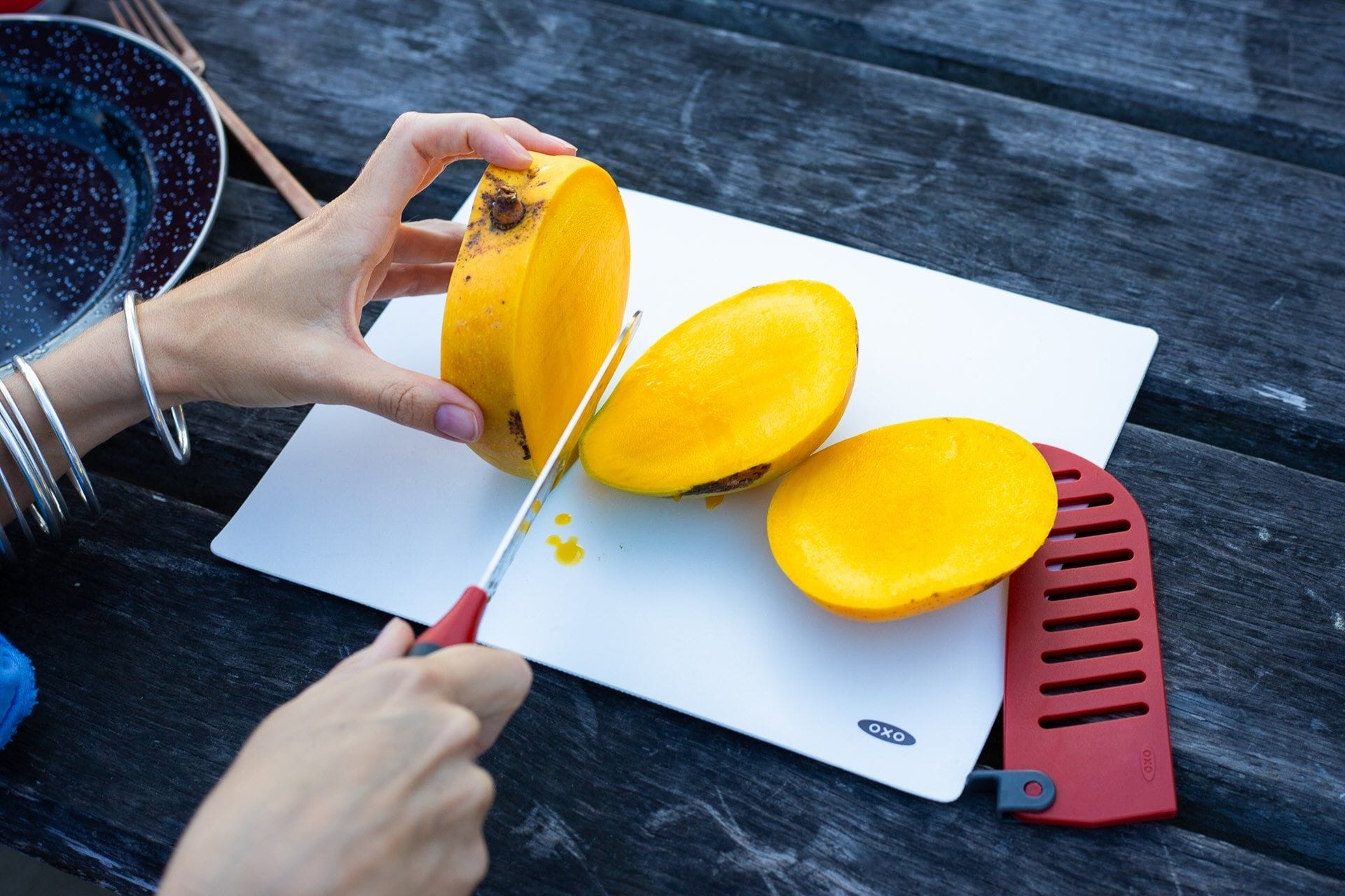 OXO camp kitchen, cutting mango, white cutting board, kitchen knife, red silicone spatula, outdoor food preparation, camping, wooden table