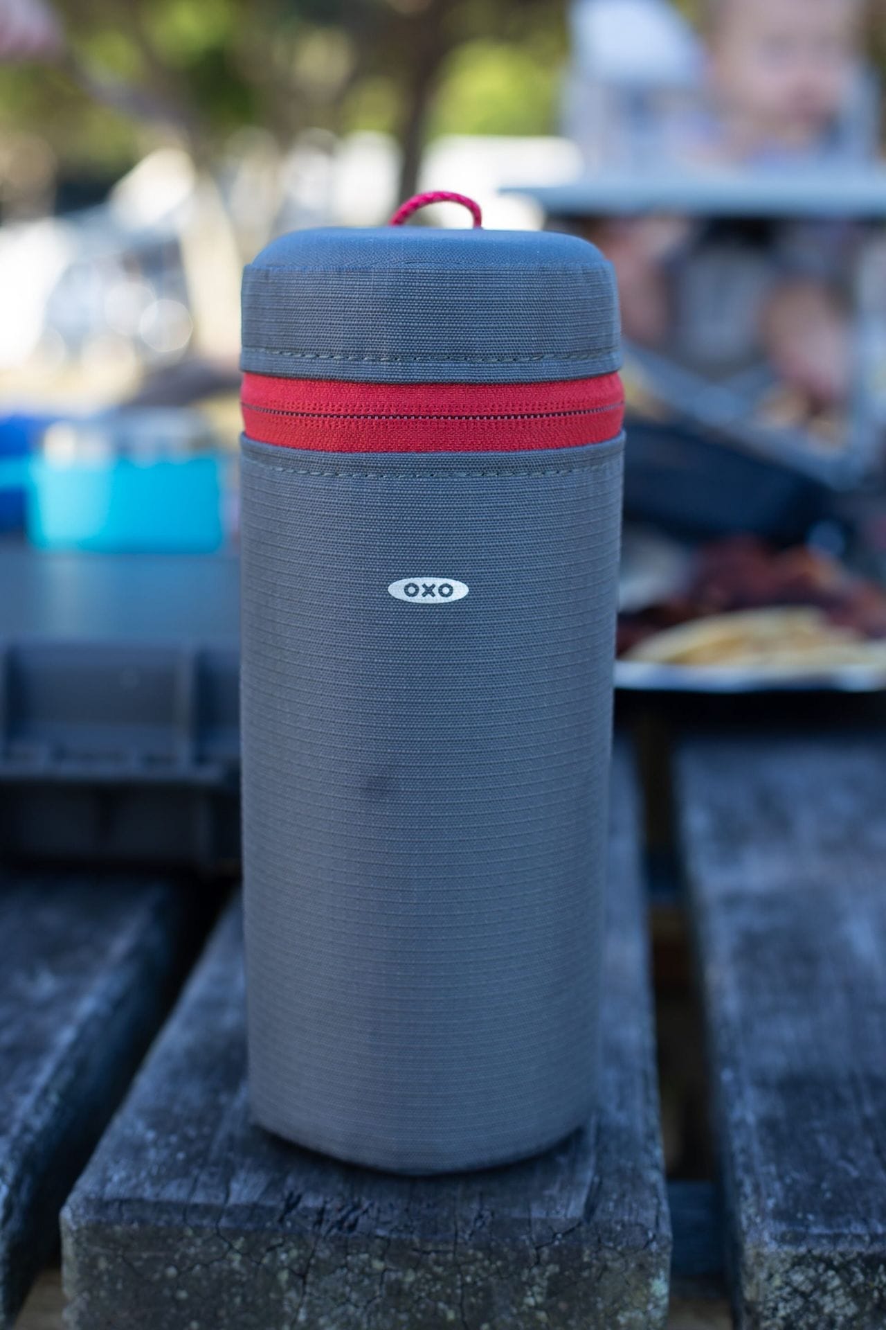 OXO Outdoor product, grey travel bag, red zipper, camping gear, wooden table, outdoor camp kitchen