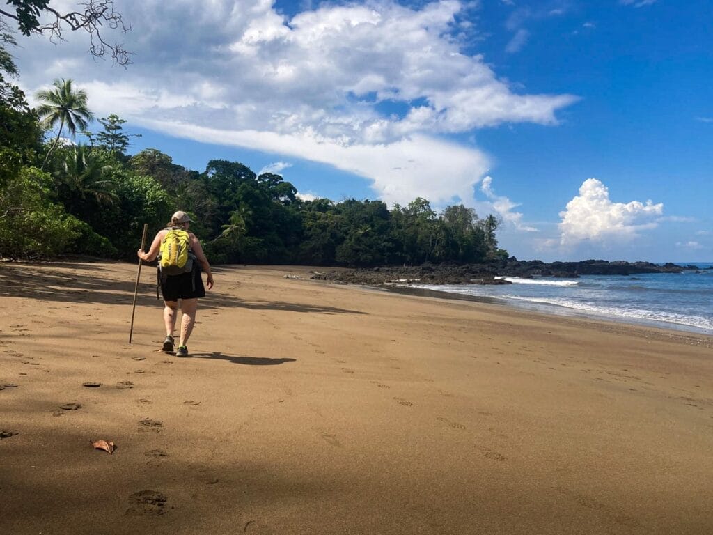 Costa Rica beach, by Andrea Salus, person walking, sandy, tropical forest, ocean, blue sky, hiking, adventure