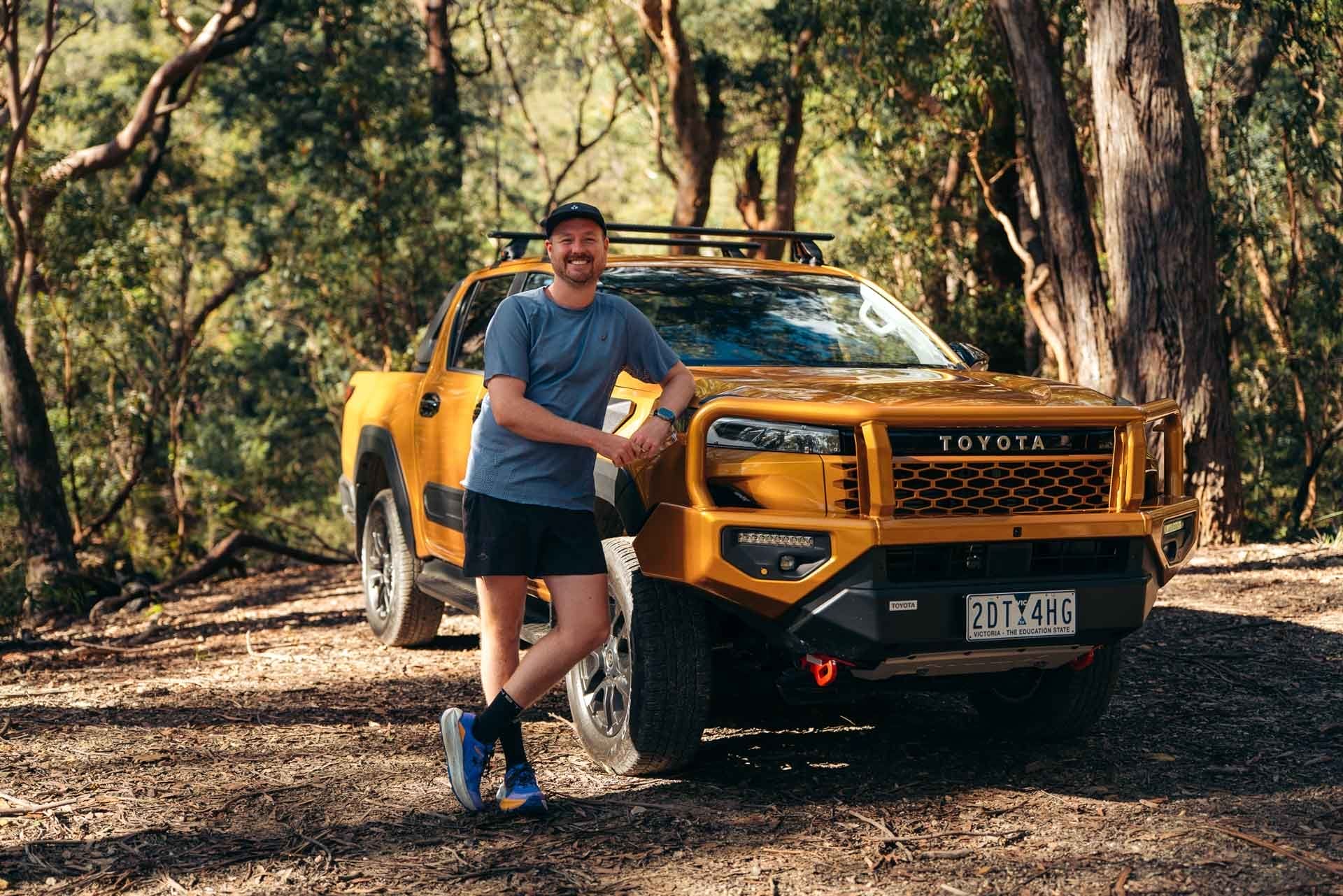 Tim (We Are Explorers) with Toyota HiLux SR5, by Paul, smiling man, golden pickup truck, Australian bush, outdoor adventure, vehicle test