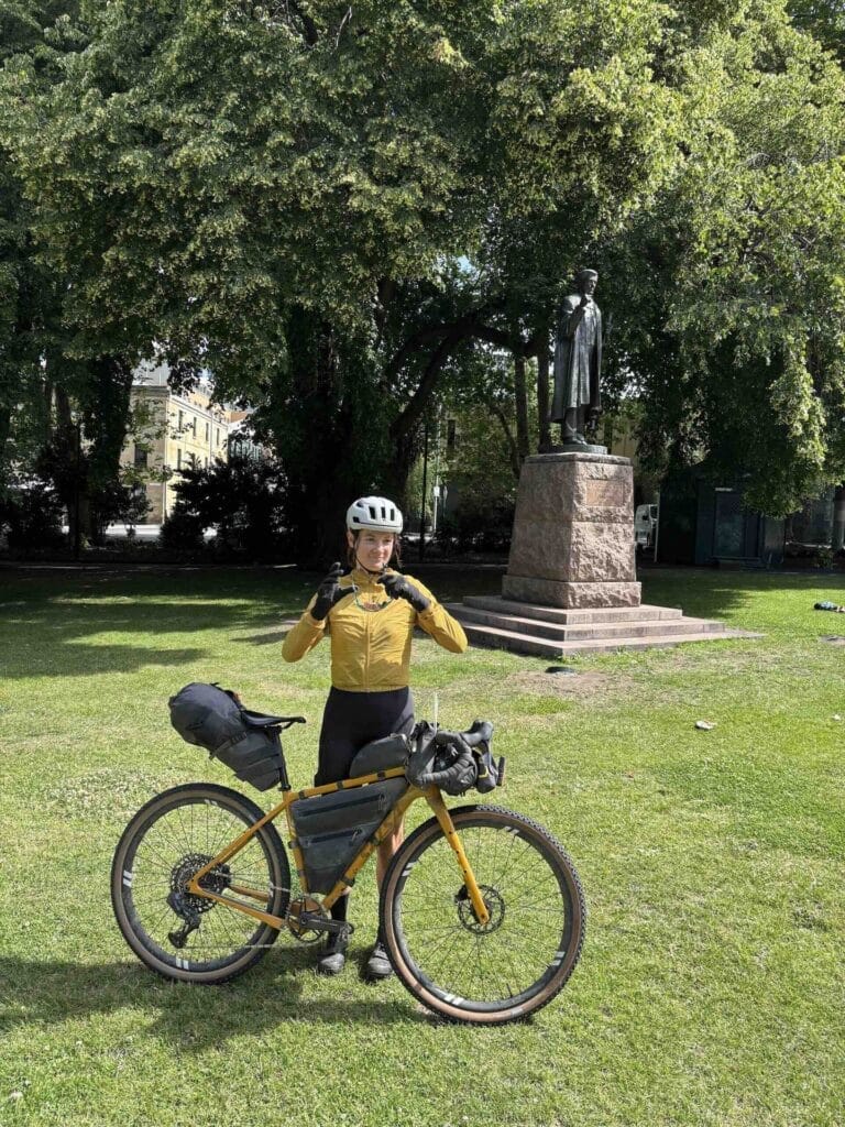 Hobart, Tassie Traverse finish, by Rohan Hunt, female cyclist, bikepacking bike, city park, bronze statue, green trees, sunny day, Tasmania cycling adventure