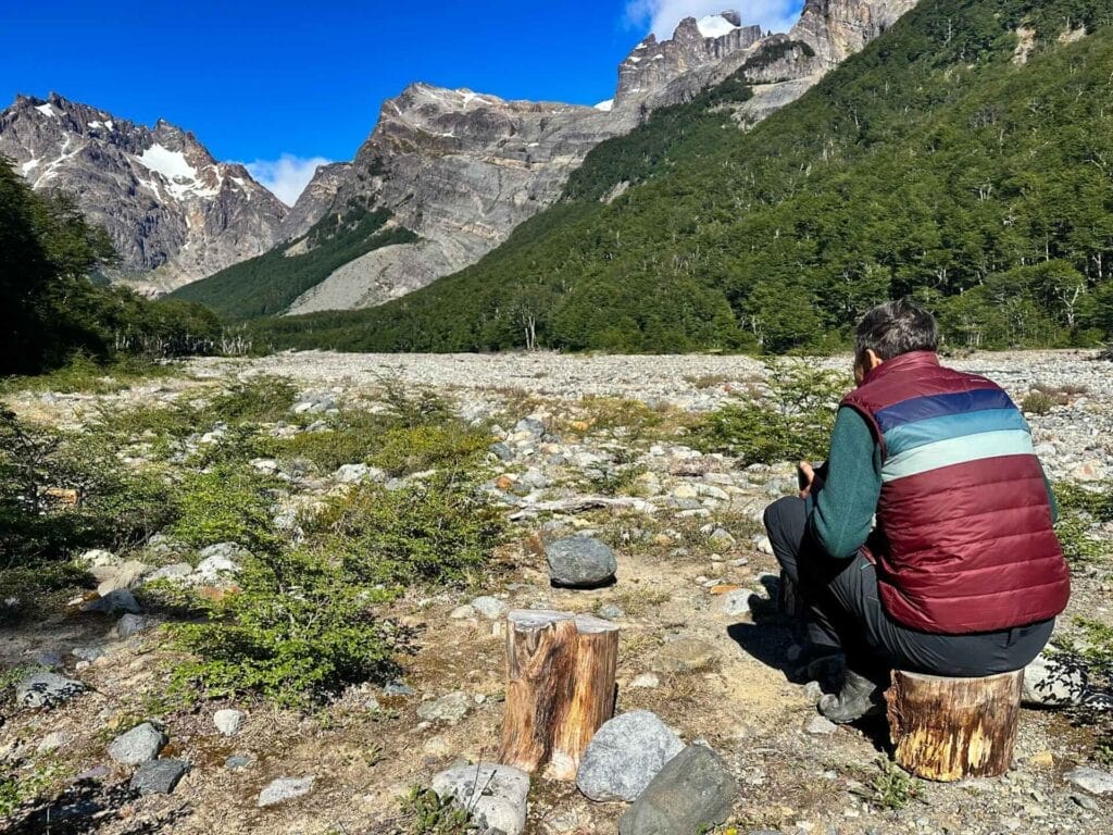 Las Horquetas Trek, Cerro Castillo National Park, Patagonia, person resting, rocky landscape, snow-capped mountains, green forests, clear blue sky, hiking break, trekking, solitude, Patagonian nature
