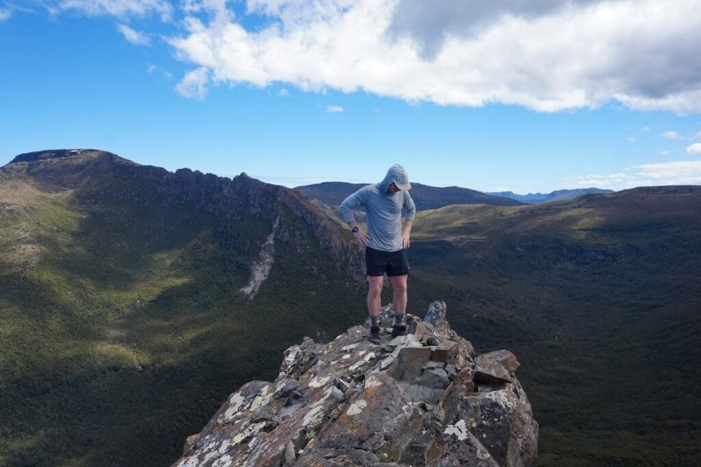 Tasmanian wilderness, mountain peak, rocky landscape, hiker, valley view, remote adventure, blue sky