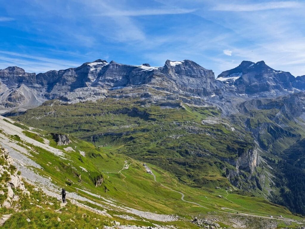 Klausen Pass, Balmer Grätli, by Beckerhoff, hiking descent, mountain range, snow-capped peaks, green slopes, winding trail, alpine landscape, blue sky, Switzerland, Swiss Alps, long-distance trek